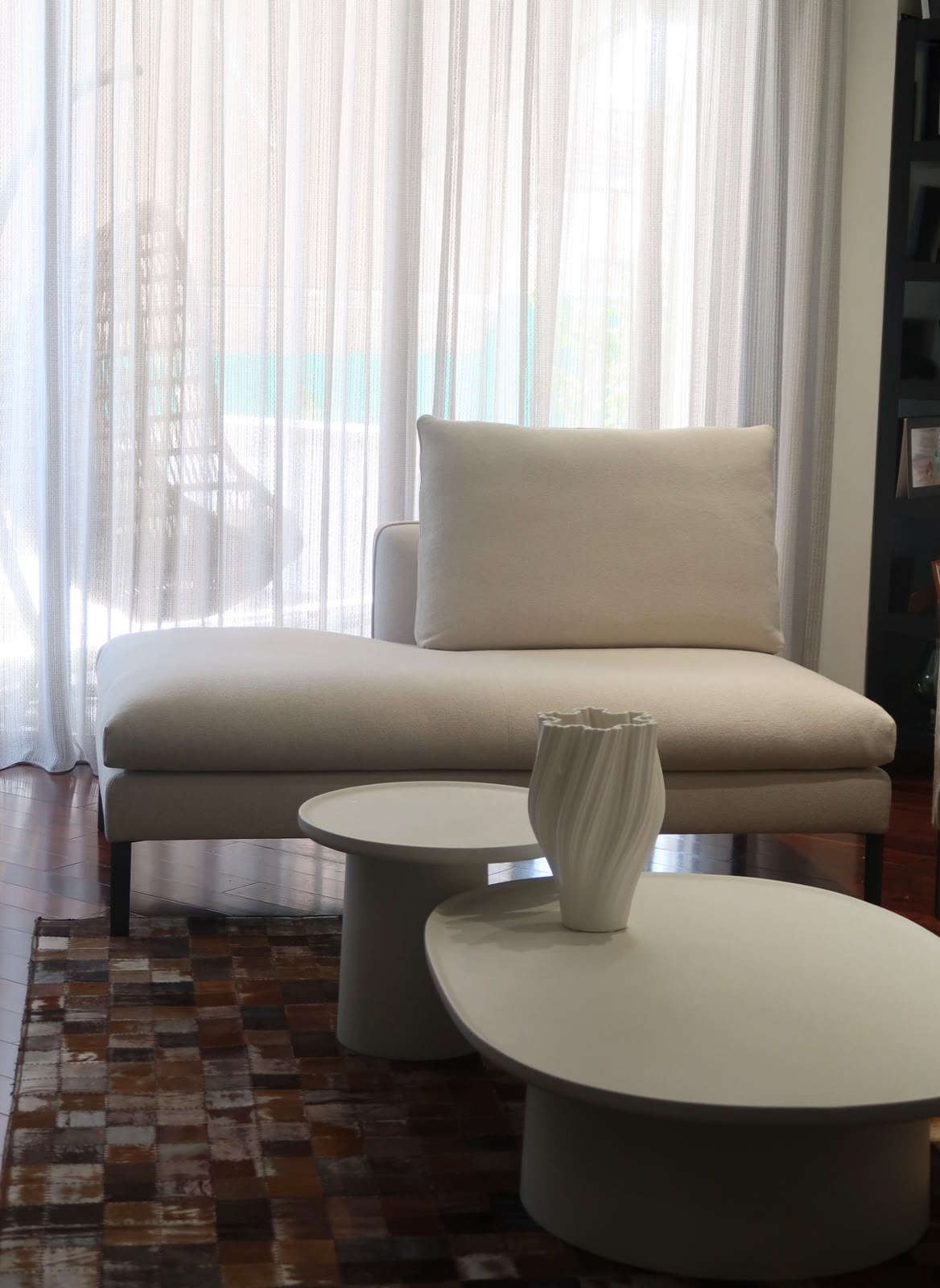 Chaise longue and nesting coffee tables in front of sheer curtains