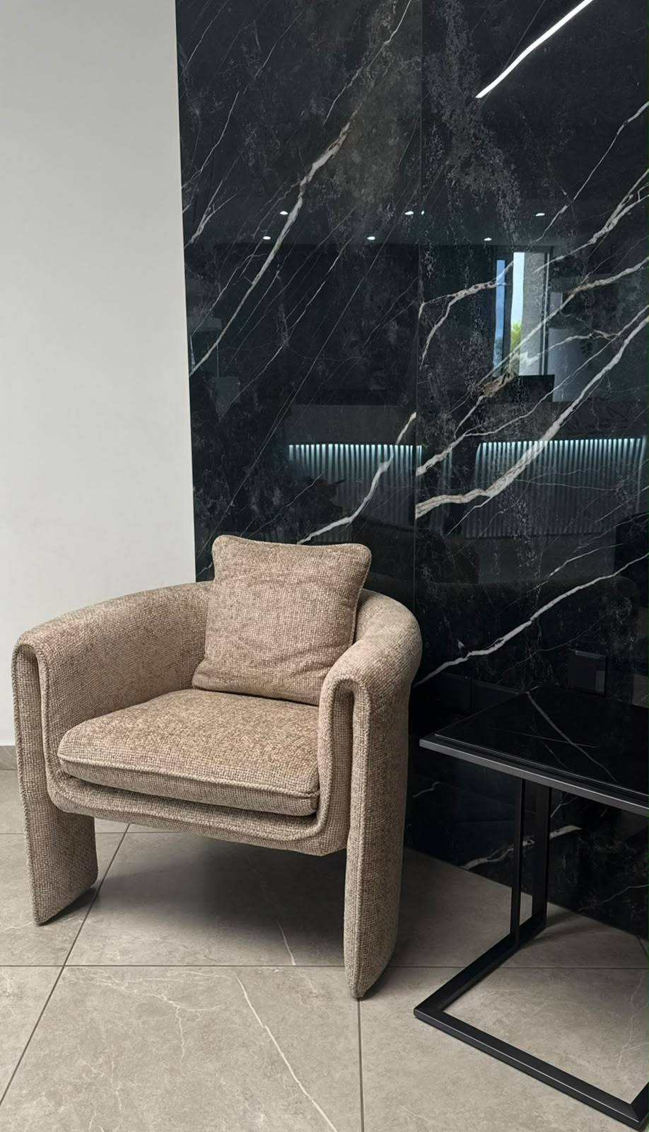 Oatmeal bouclé armchair in front of a black marble wall
